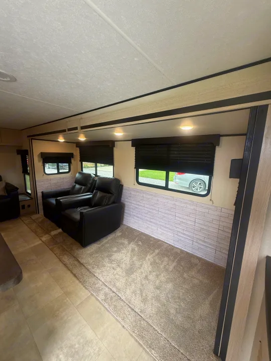 Experience comfort in this RV rental living area: black recliners, window views, and a mix of carpet and tile flooring.. Coachmen Apex 2021