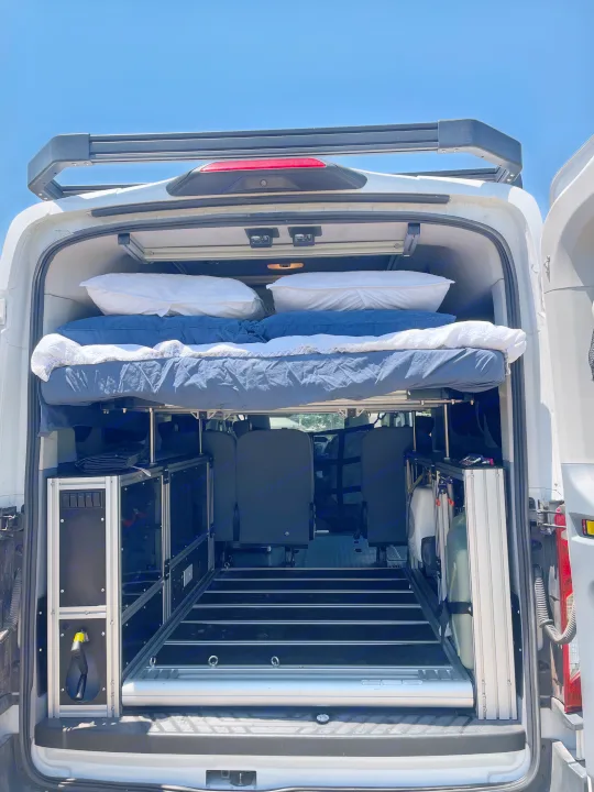 RV rental van conversion: Rear view shows a comfy raised bed, modular storage, and versatile interior layout.. Ford Transit 2018