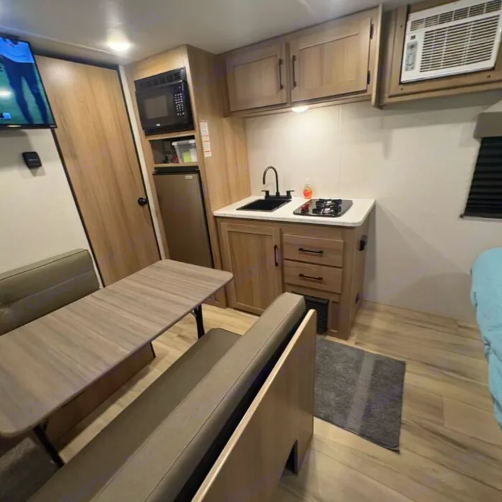 This inviting RV rental interior features a dinette, compact kitchenette with sink & stove, microwave, fridge, and AC unit.. Keystone RV Coleman 2025