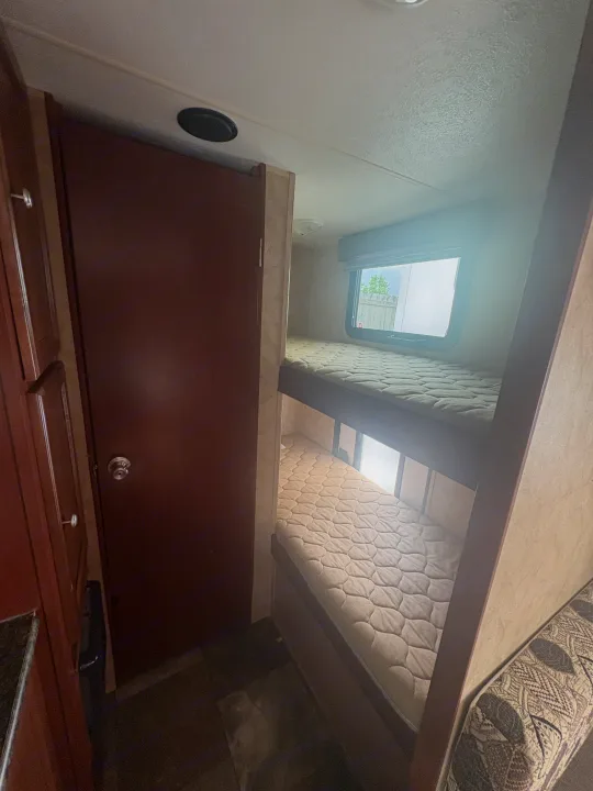 Compact RV rental interior featuring cozy bunk beds and a nearby door, ideal for a family getaway.. Coachmen Clipper 17BH 2015