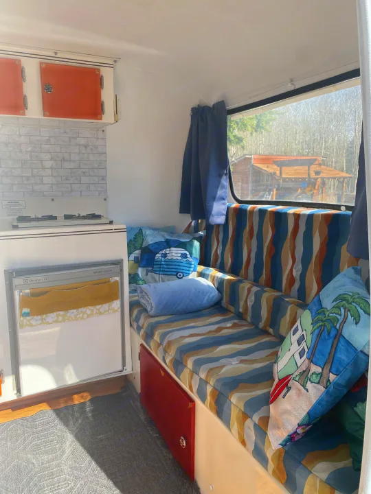 RV rental interior with a compact kitchen, colorful seating, and window view of nature through closed curtains.. Scamp 13' 1987