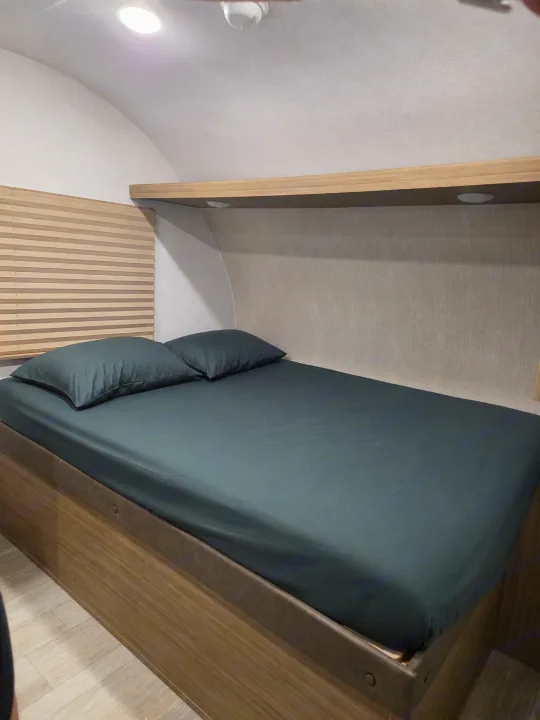 Cozy rv rental bedroom with dark sheets, a wooden shelf with lights, and window blinds for comfort.. Forest River Salem 2026