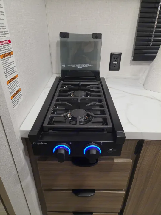 This RV rental's kitchen features a Greystone gas stovetop with two burners, blue-lit control knobs, and a glass cover.. Forest River Salem 2026