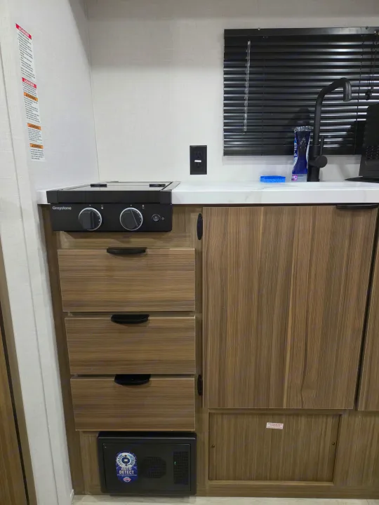 RV rental kitchen showing a Greystone stovetop, sink, wood cabinets, and WFCO power center.. Forest River Salem 2026