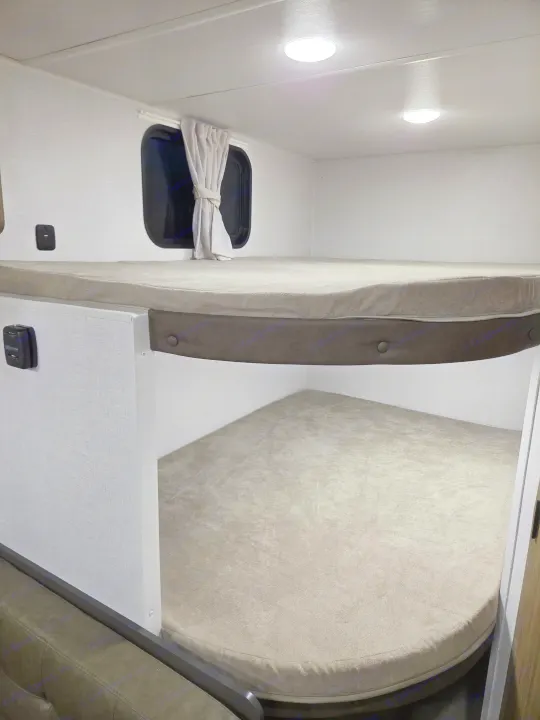 RV rental interior: light-colored bunk beds with mattresses, a window, and ceiling lights, creating a comfortable sleeping area.. Forest River Salem 2026
