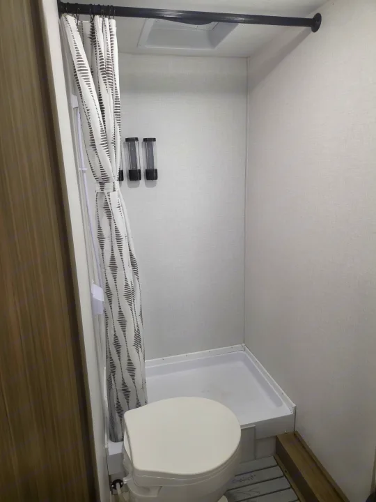 Compact RV rental bathroom: features a toilet, shower stall, patterned curtain, and soap dispensers.. Forest River Salem 2026