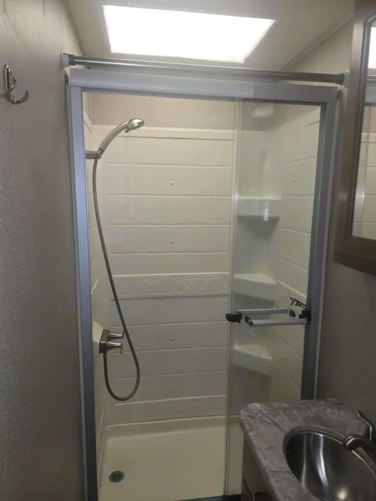 Bright RV rental bathroom. Features a shower with sliding glass door, a handheld shower head, and a counter with sink.. Entegra Coach Vision 2019
