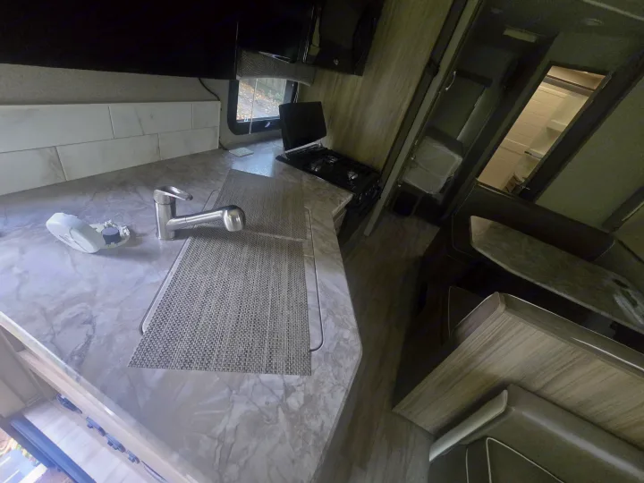 RV rental kitchen & dining area with countertop, sink, stovetop, backsplash, and dining booth. A detector is open on the counter.. Entegra Coach Vision 2019