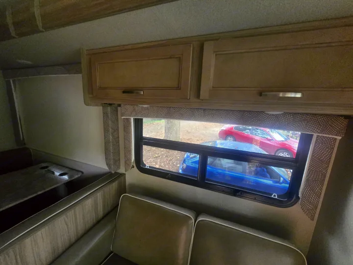 Cozy RV rental interior: dinette seating, window with a view of cars outside, and light wood cabinetry above.. Entegra Coach Vision 2019