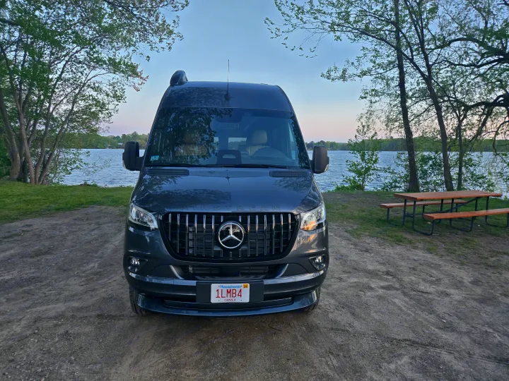 A sleek Mercedes Sprinter campervan, ready for your RV rental getaway, parked lakeside next to a picnic table.. Airstream Interstate 2026