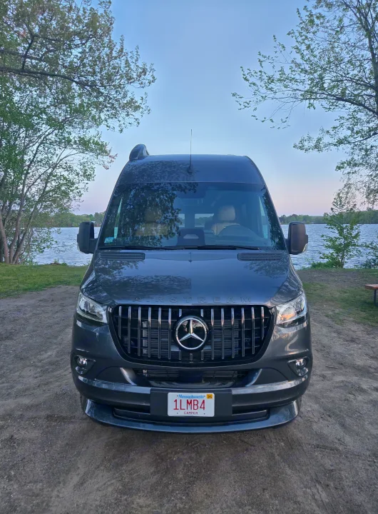 Dark gray Airstream rv rental camper van parked by a lake under a clear sky, surrounded by trees. Ideal for outdoor adventures.. Airstream Interstate 2026