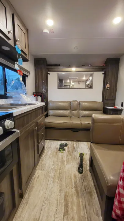 RV rental interior featuring a full kitchen with sink/stove, comfy sofa, dinette, wood flooring, and bright overhead lights.. Highland Ridge RV Open Range 2020