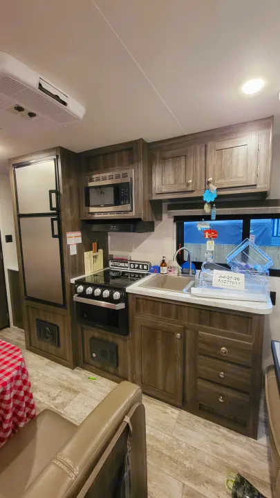 Modern RV rental kitchen featuring a fridge, microwave, stove, sink, and wood-look cabinets for a cozy travel experience.. Highland Ridge RV Open Range 2020