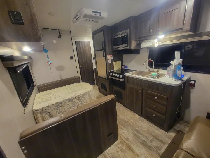 A cozy rv rental living space with a kitchen featuring a microwave, stove, and sink, plus a dining booth with benches.. Highland Ridge RV Open Range 2020