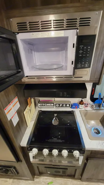 RV rental kitchen with open microwave, gas stovetop, and sink for cooking convenience.. Highland Ridge RV Open Range 2020