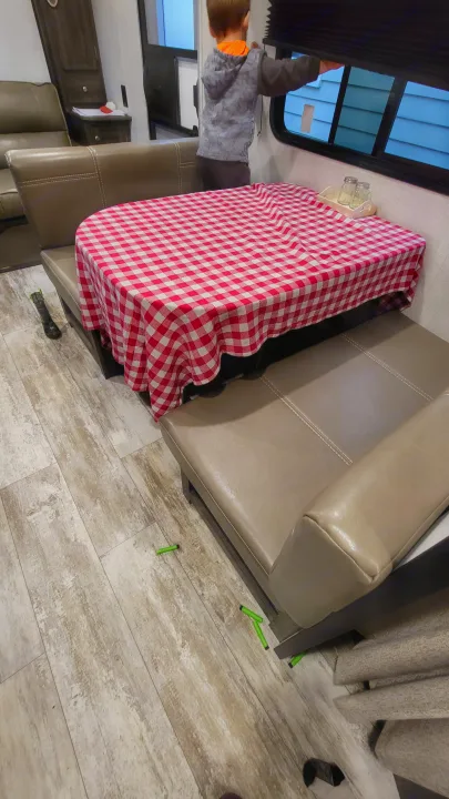 Child opens window blind in RV rental dinette area. Red checkered tablecloth, shakers, and playful items on floor.. Highland Ridge RV Open Range 2020