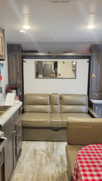 Cozy RV rental interior with a sofa, kitchen, dining nook, and overhead storage. Photographer reflected in the mirror.. Highland Ridge RV Open Range 2020