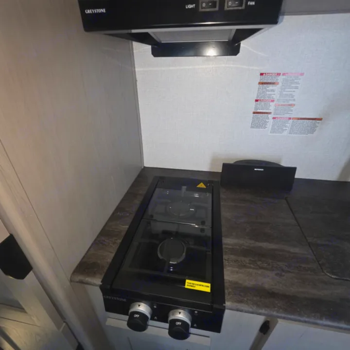 RV rental kitchen: Greystone 2-burner cooktop, range hood, and a speaker on the dark countertop, ready for your adventure.. Clipper 5K 2024