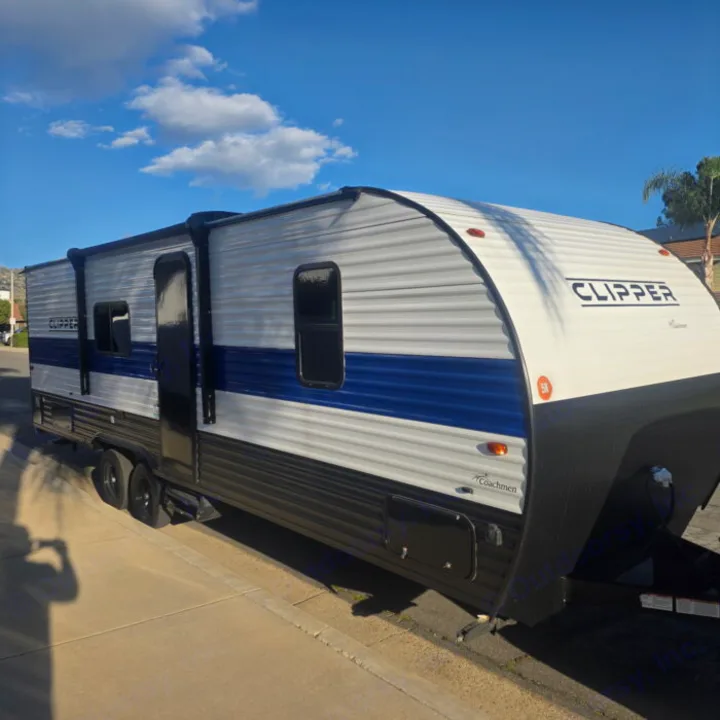 A white and blue Clipper travel trailer, a perfect rv rental for scenic road trips. Parked on a sunny street.. Clipper 5K 2024