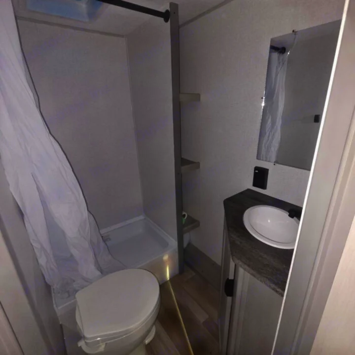 Inside a clean RV rental bathroom, featuring a toilet, small shower, and a vanity with sink and mirror.. Clipper 5K 2024