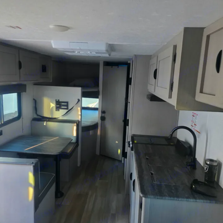 Explore this RV rental interior, featuring a compact kitchen with a sink, a cozy dinette, and visible bunk beds for travel comfort.. Clipper 5K 2024