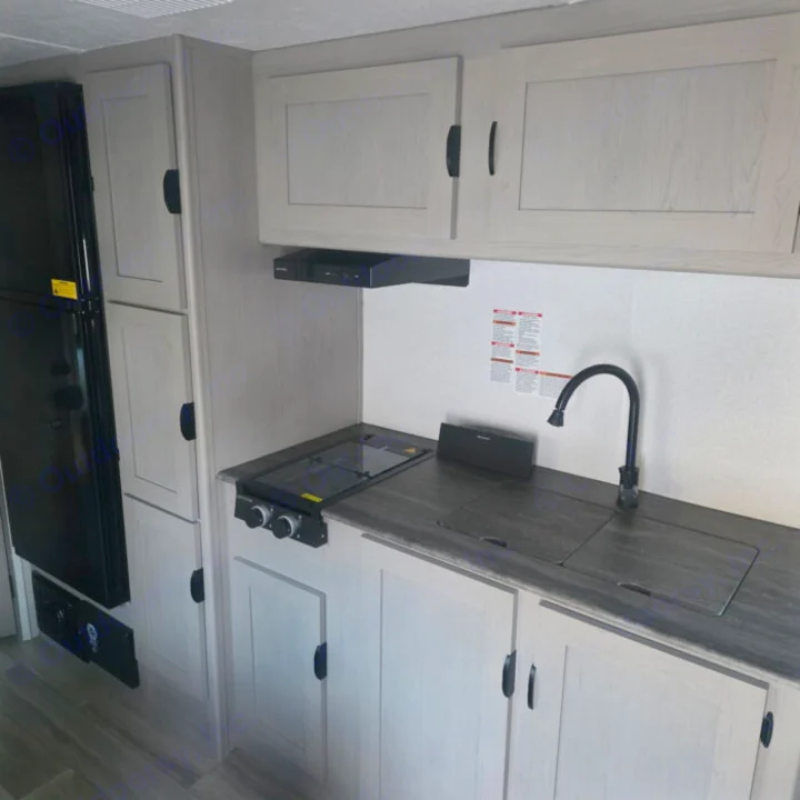 Compact RV rental kitchen with light cabinets, dark counters, sink, stovetop, and large refrigerator. Perfect for travel!. Clipper 5K 2024