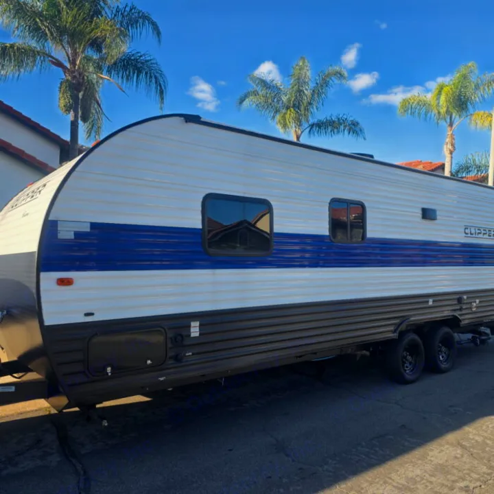 A large white and blue Clipper travel trailer, ideal for an RV rental adventure, parked on pavement with palm trees overhead.. Clipper 5K 2024
