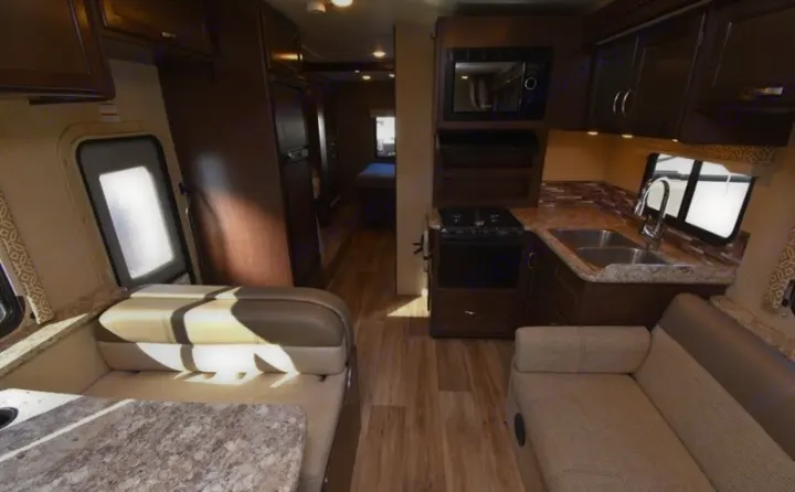 Cozy rv rental interior featuring a kitchen with sink, stove, microwave, dinette, and couch. Bedroom visible in the back.. Thor Freedom Elite 2017
