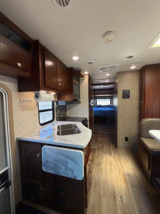 Spacious RV rental interior featuring a full kitchen with double sinks, stove, and microwave, leading to a cozy bedroom.. Forest River Sunseeker 2017
