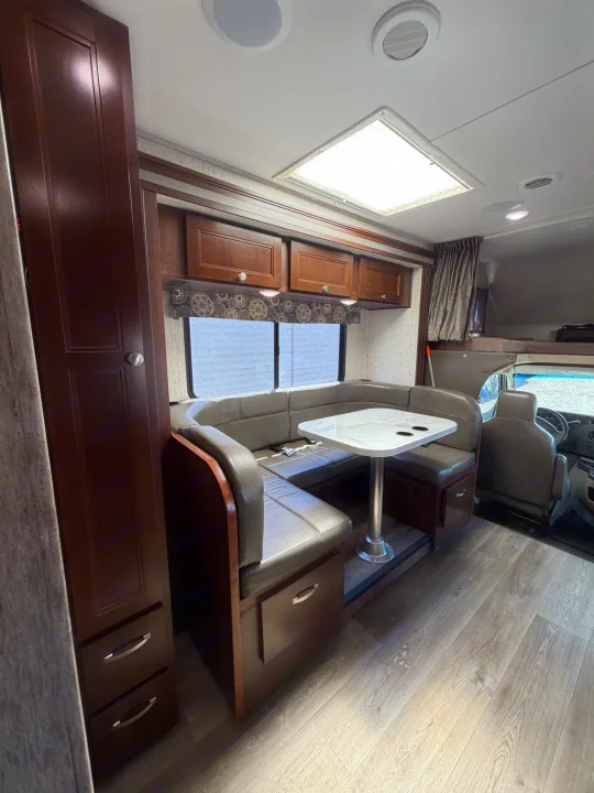 Interior of an RV rental showing a U-shaped dining booth, table, overhead cabinets, and front bunk area.. Forest River Sunseeker 2017