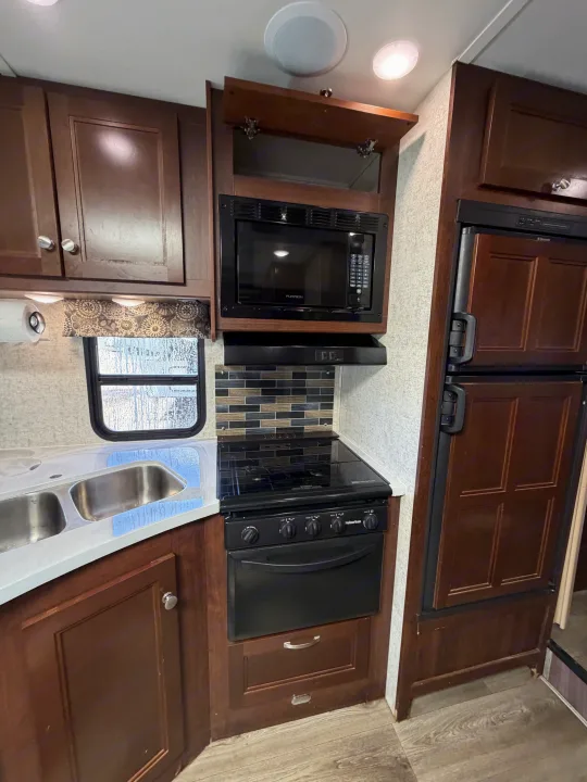 Modern rv rental kitchen featuring a microwave, stovetop, dual sink, and refrigerator within dark wood cabinetry.. Forest River Sunseeker 2017