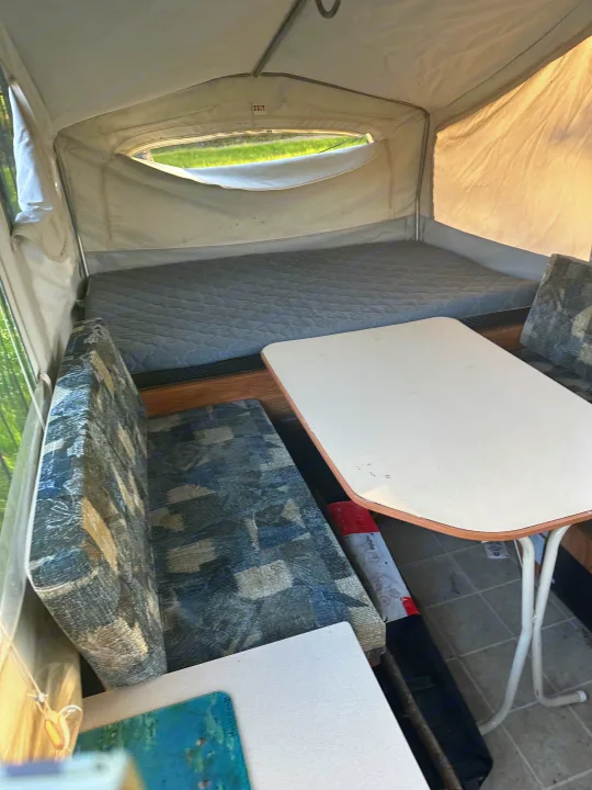 Cozy RV rental pop-up camper interior with a comfy bed, patterned dinette, and table. Canvas walls and a window for scenic views.. Jayco Qwest 2004