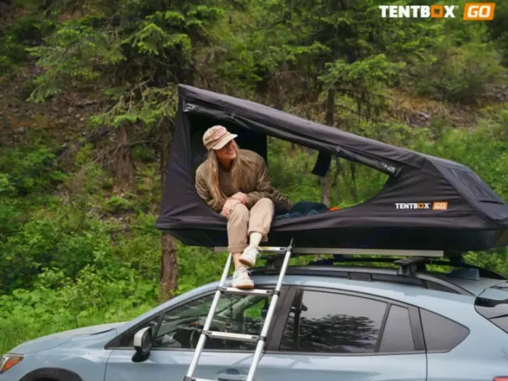 A woman relaxes in a car-top tent on a vehicle, an ideal camping solution for outdoor adventure, similar to an RV rental.. TENTBOX GO 2026