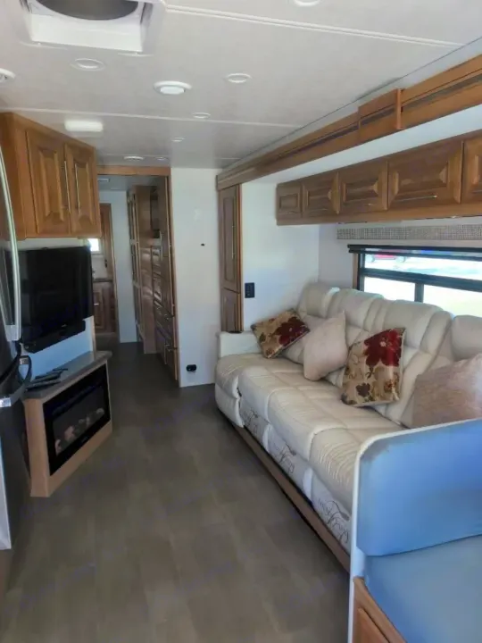 This rv rental features a bright living area with a plush cream sofa, decorative pillows, TV, electric fireplace, and ample wood storage.. Forest River GEORGETOWN 36D7 2024