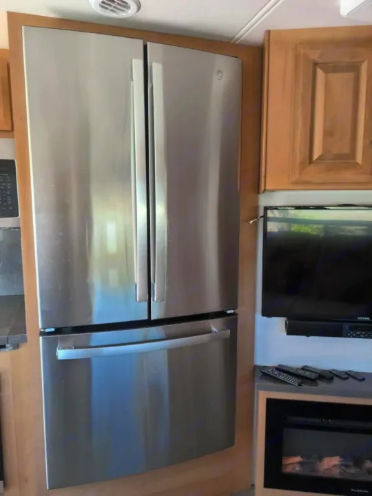 RV rental interior: modern stainless steel French door refrigerator, adjacent TV, and electric fireplace in compact design.. Forest River GEORGETOWN 36D7 2024