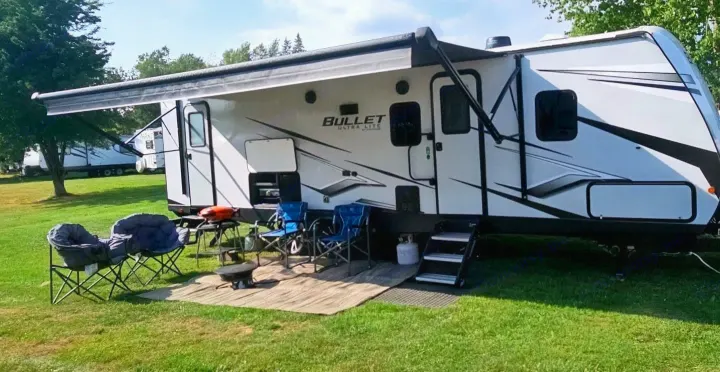 Bullet Ultra Lite RV rental parked at a sunny campsite with an extended awning, chairs, and grill setup for outdoor relaxation.. Keystone RV Bullet Ultra Lite 2023