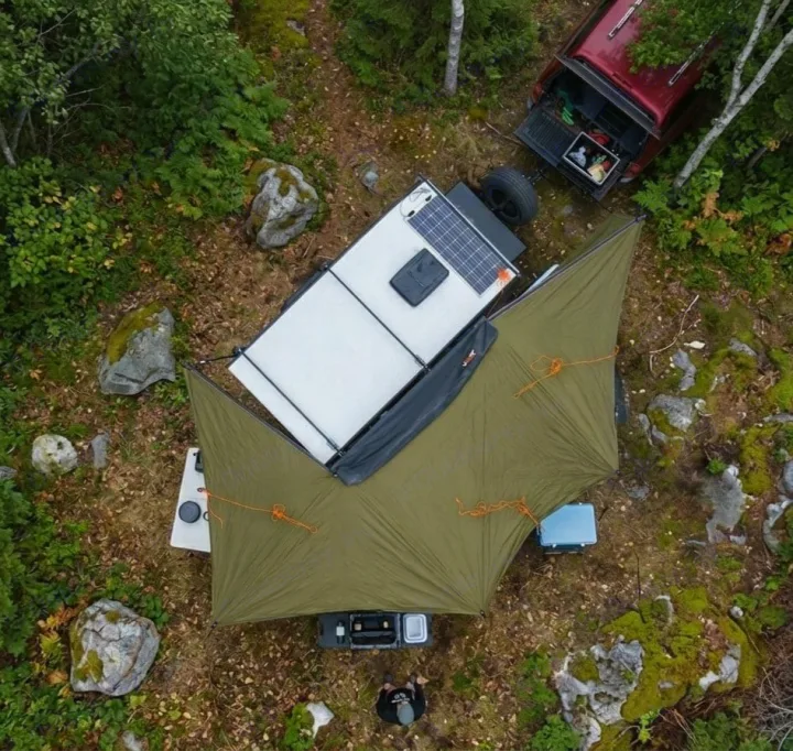 Overhead view of an RV rental setup: a pickup truck and an overlanding trailer with solar panels and a tarp in a forest campsite.. Hiker Trailer Backcountry Trailer (Mid Range XL) 2022