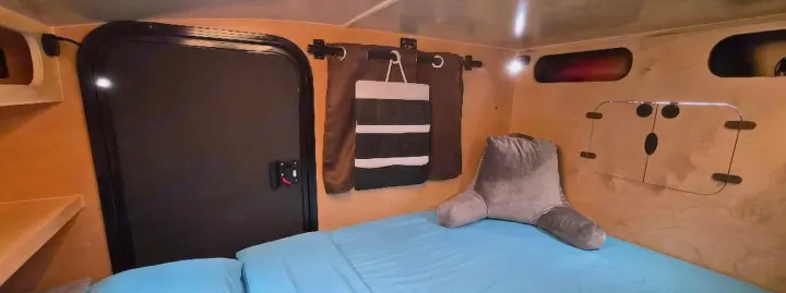 RV rental interior: cozy bed with back pillow, wood paneling, storage cubbies, and a door for your next camper adventure.. Hiker Trailer Backcountry Trailer (Mid Range XL) 2022