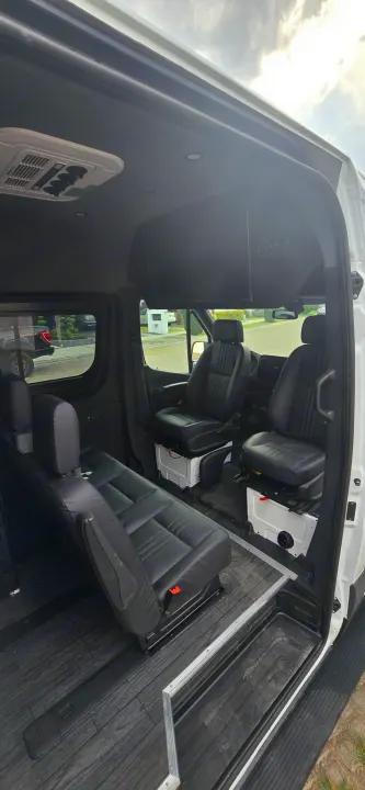 Spacious, customized RV rental van interior with black leather seats, wood-look floor, and AC for comfortable travel.. Mercedes Sprinter 2023