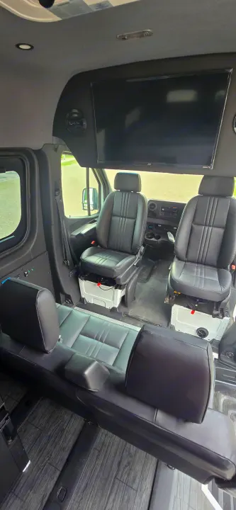 Modern rv rental van interior: black leather captain chairs, rear bench, Roku TV, and wood-style floor.. Mercedes Sprinter 2023