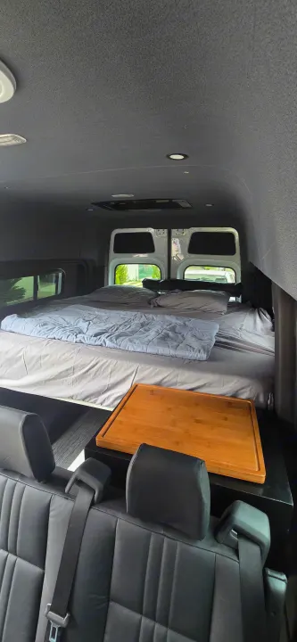 Cozy rv rental interior: elevated sleeping area, bedding, and wooden tray. Ideal for camper van adventures.. Mercedes Sprinter 2023