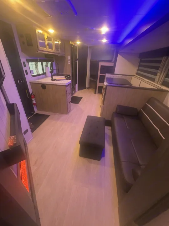 Modern rv rental interior: kitchen, dining booth, sofa, and bunks with vibrant blue and warm lighting.. Forest River 26KF 2026