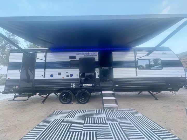 Cherokee Grey Wolf rv rental travel trailer, featuring an extended awning with blue LED lights & an outdoor kitchen, ready for camping.. Forest River 26KF 2026