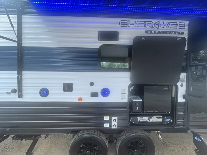 Side view of a Cherokee Grey Wolf RV rental with blue LED awning lights and an open outdoor kitchen, including a TV and grill.. Forest River 26KF 2026