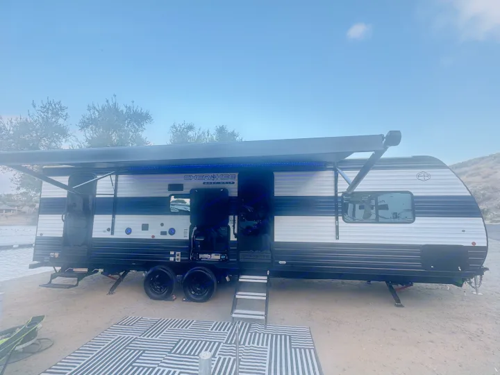 A Cherokee Grey Wolf **rv rental** parked lakeside with its awning extended and outdoor mat. Ideal for a scenic getaway.. Forest River 26KF 2026