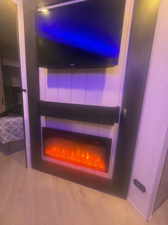 Cozy RV rental interior with a TV, soundbar, and an inviting electric fireplace. Adjacent bedroom space is visible.. Forest River 26KF 2026