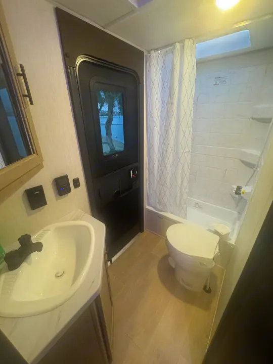 This RV rental bathroom features a sink, toilet, and shower/tub, with a door offering a scenic outdoor view.. Forest River 26KF 2026