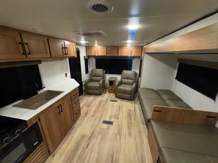 This modern rv rental interior features a kitchen, two recliners, and a sofa. Light wood cabinets and floor create a bright space.. Keystone RV Other 2026