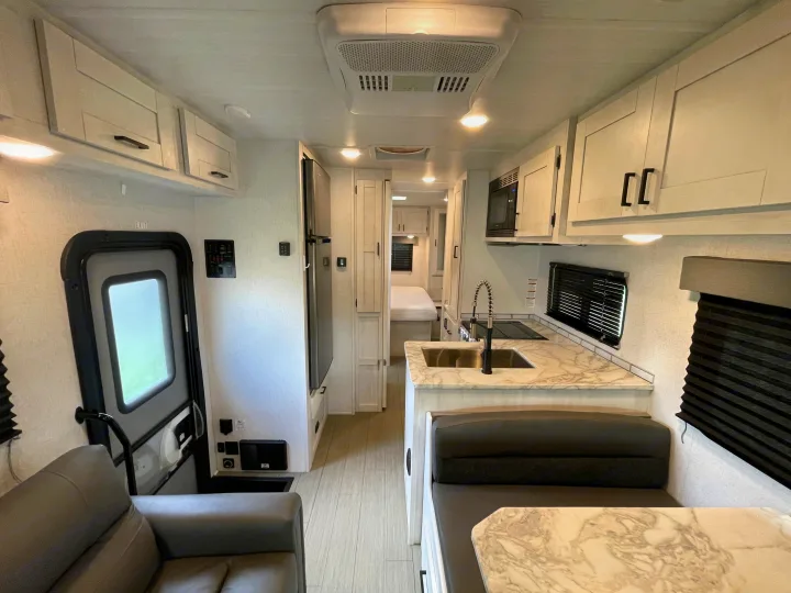 Bright, modern RV rental interior with a fully equipped kitchen, dinette, and cozy sofa, leading to a rear bedroom.. Entrada Entrada Motorhome 2022