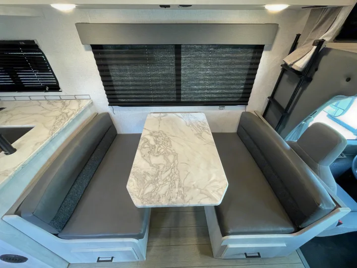 rv rental: Interior view of a clean RV dinette with a faux-marble table, gray upholstered benches, a kitchen area, and a bunk ladder.. Entrada Entrada Motorhome 2022